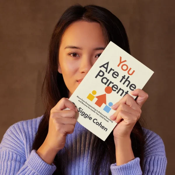 A woman holding up You Are The Parent by Dr. Siggie Cohen in front of her face