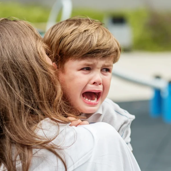 Parent holding a crying, dysregulated child outdoors, using calm physical presence to provide comfort and containment