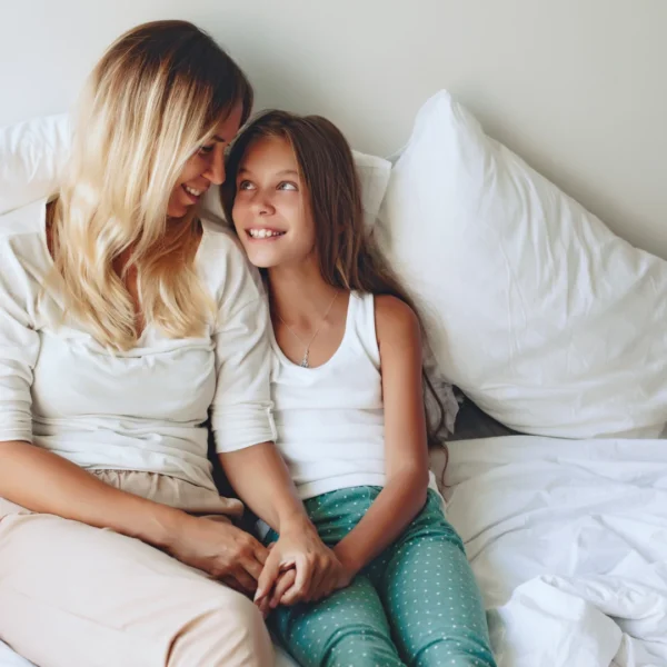 Smiling mother and preteen daughter holding hands on a bed, the kind of connection the best parenting advice is built on