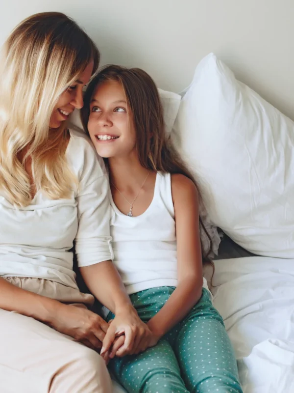 Smiling mother and preteen daughter holding hands on a bed, the kind of connection the best parenting advice is built on